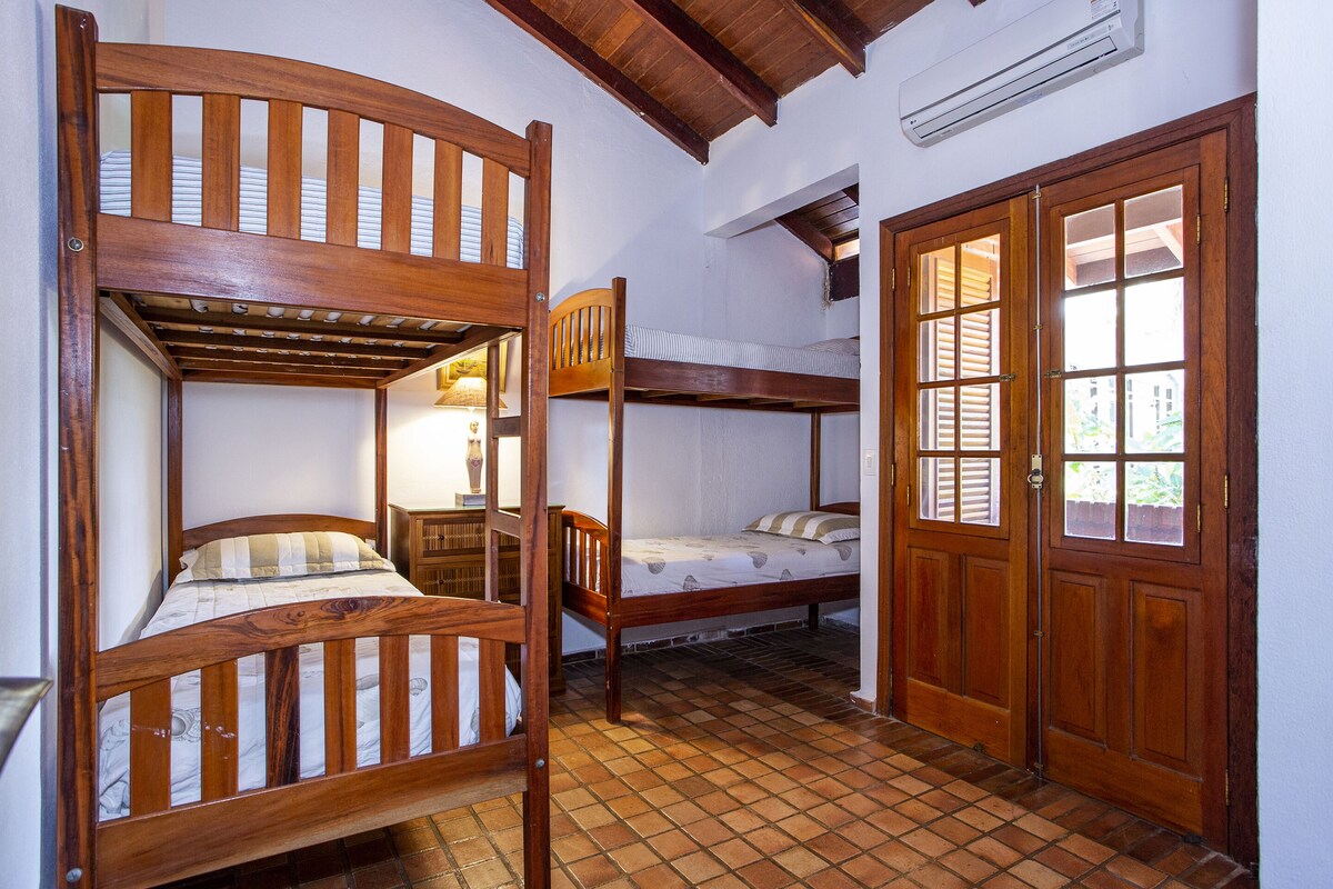 A room with two wooden bunk beds, a wooden door with glass panels, and a tiled floor.