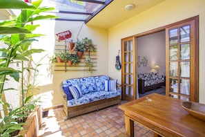 A sunlit patio with a wicker sofa, wooden table, and potted plants. - Residencial Santa Lucia (São Sebastião)