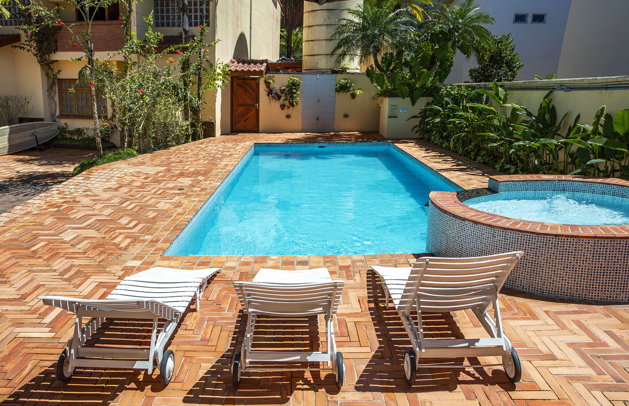 Une piscine rectangulaire avec un jacuzzi, entourée d’une terrasse en briques agrémentée de chaises longues.