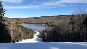 A snow-covered landscape with a clear sky, a frozen lake, and a path leading to a cabin. - Slopeside ski in/out 1 bedroom condo with parking on site! (Snowshoe)