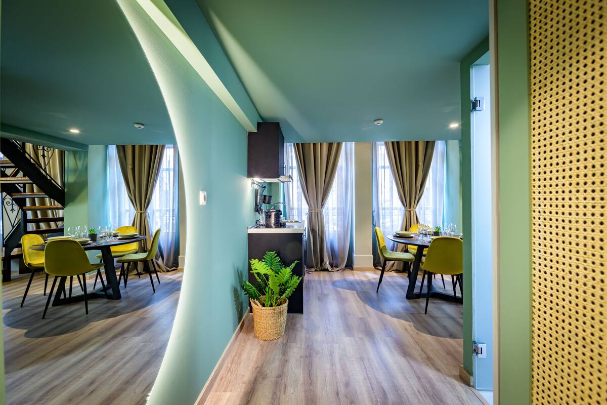 A modern dining area with wooden flooring, yellow chairs, and a central table with a potted plant.