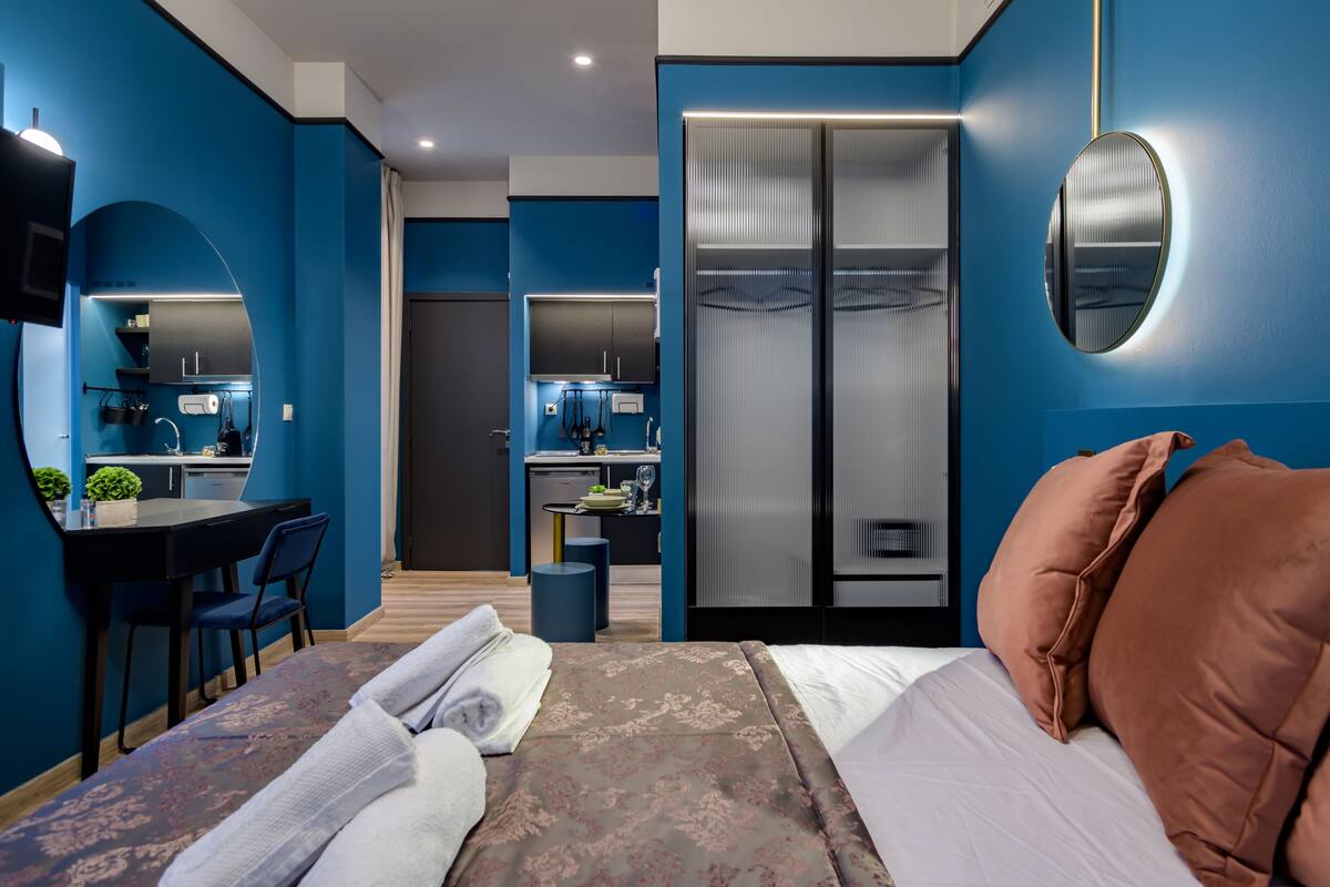 A modern hotel room with a bed, a desk, and a kitchenette.