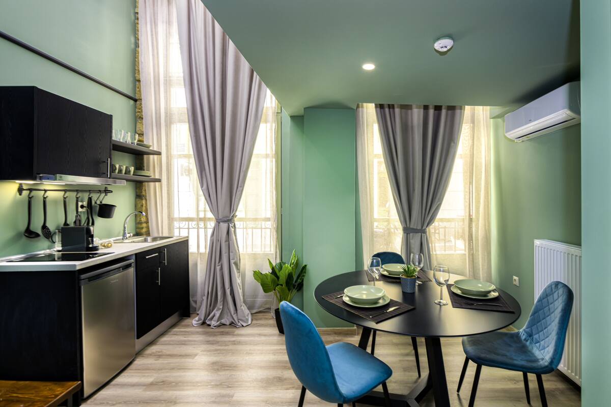 A modern kitchen with a dining area, featuring a black countertop, stainless steel appliances, and a round dining table with blue chairs.