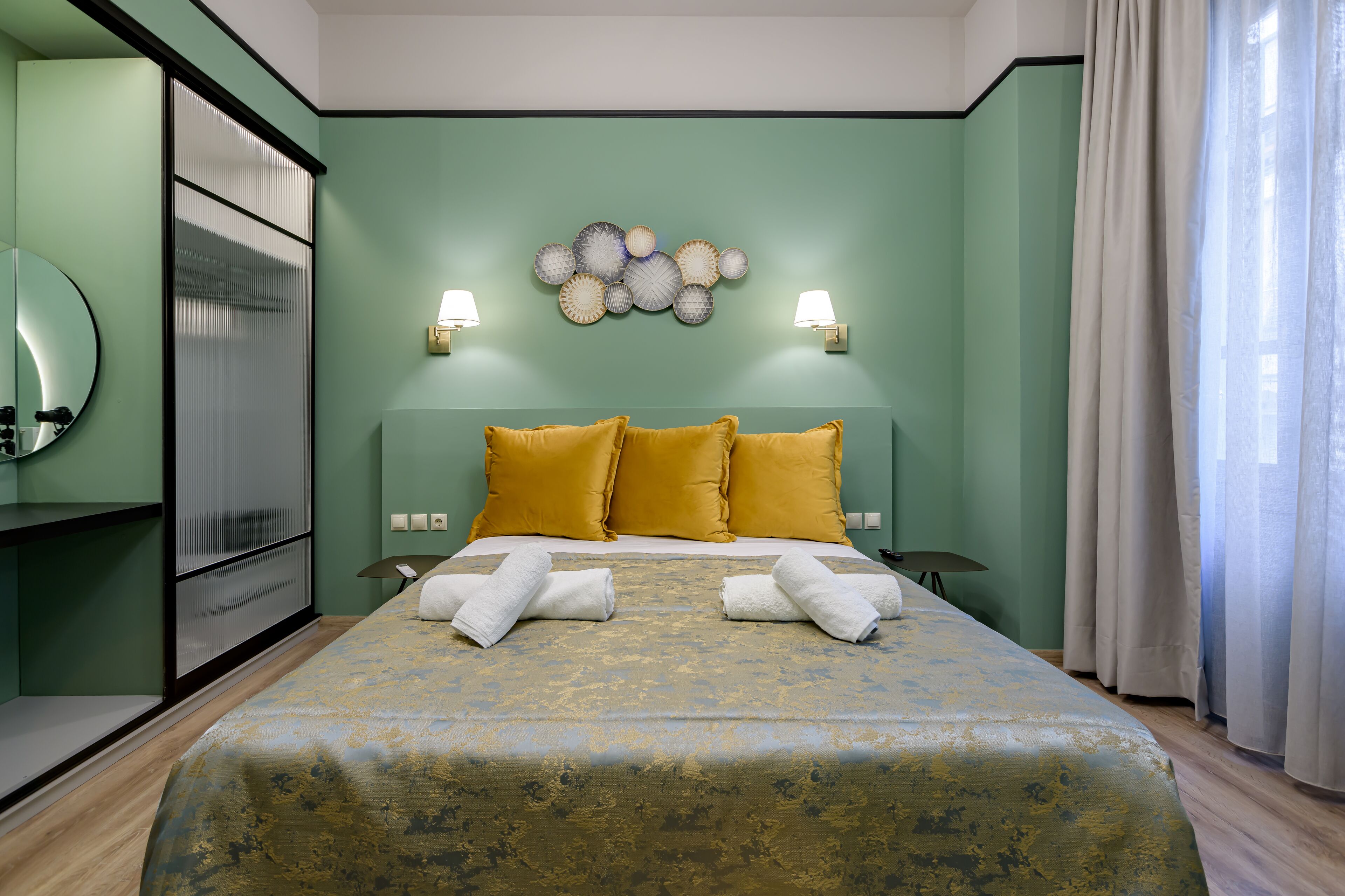 Cama bem arrumada com almofadas amarelas, um objeto decorativo na parede e duas luminárias fixadas na parede.