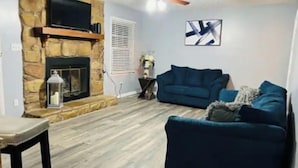 A living room with a stone fireplace, a blue sofa, a wooden floor, and a ceiling fan. - Fayetteville, NC, close to I-295 and Fort Bragg (Fayetteville)