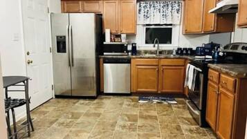 Eine kleine Küche mit Holzschränken, einem Edelstahlkühlschrank, einer Spülmaschine und einer Kaffeemaschine.