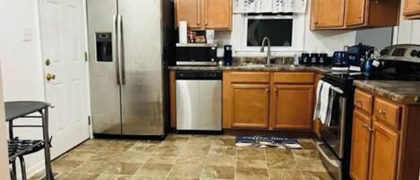 Una cocina compacta con armarios de madera, un refrigerador de acero inoxidable, un lavavajillas y una cafetera.