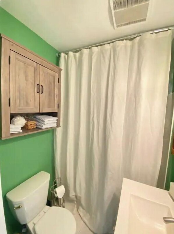A bathroom with a toilet, a cabinet with towels, and a shower curtain.