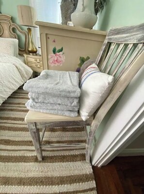 Un dormitorio con cama, una silla, toallas dobladas, un tocador y un espejo.
