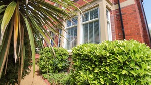 A red brick building with white window frames and shutters, surrounded by green foliage and a palm tree. - Orchard Lodge (Lytham St. Anne's)