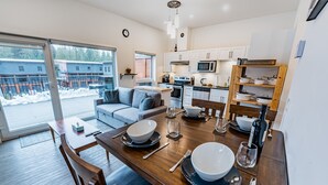 A modern kitchen with white cabinets, a dining table set for four, and a view of a snowy outdoor area.