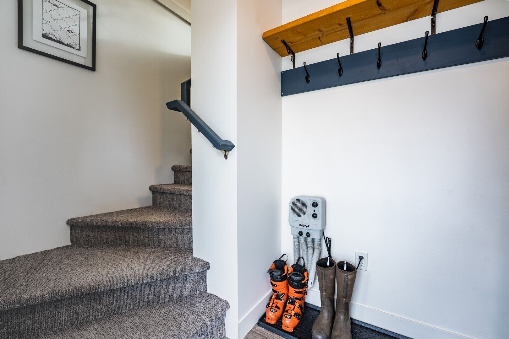A staircase with a handrail, a wall-mounted heater, and a coat rack with hooks.