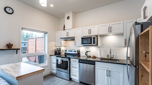 A modern kitchen with white cabinetry, stainless steel appliances, and a window overlooking a brick wall.