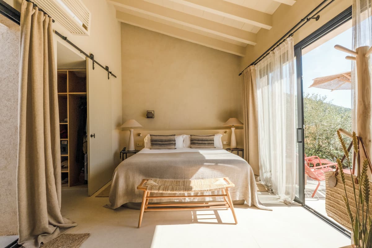 A bedroom with a large bed, a wooden bench, a closet, and a sliding glass door to the outside.