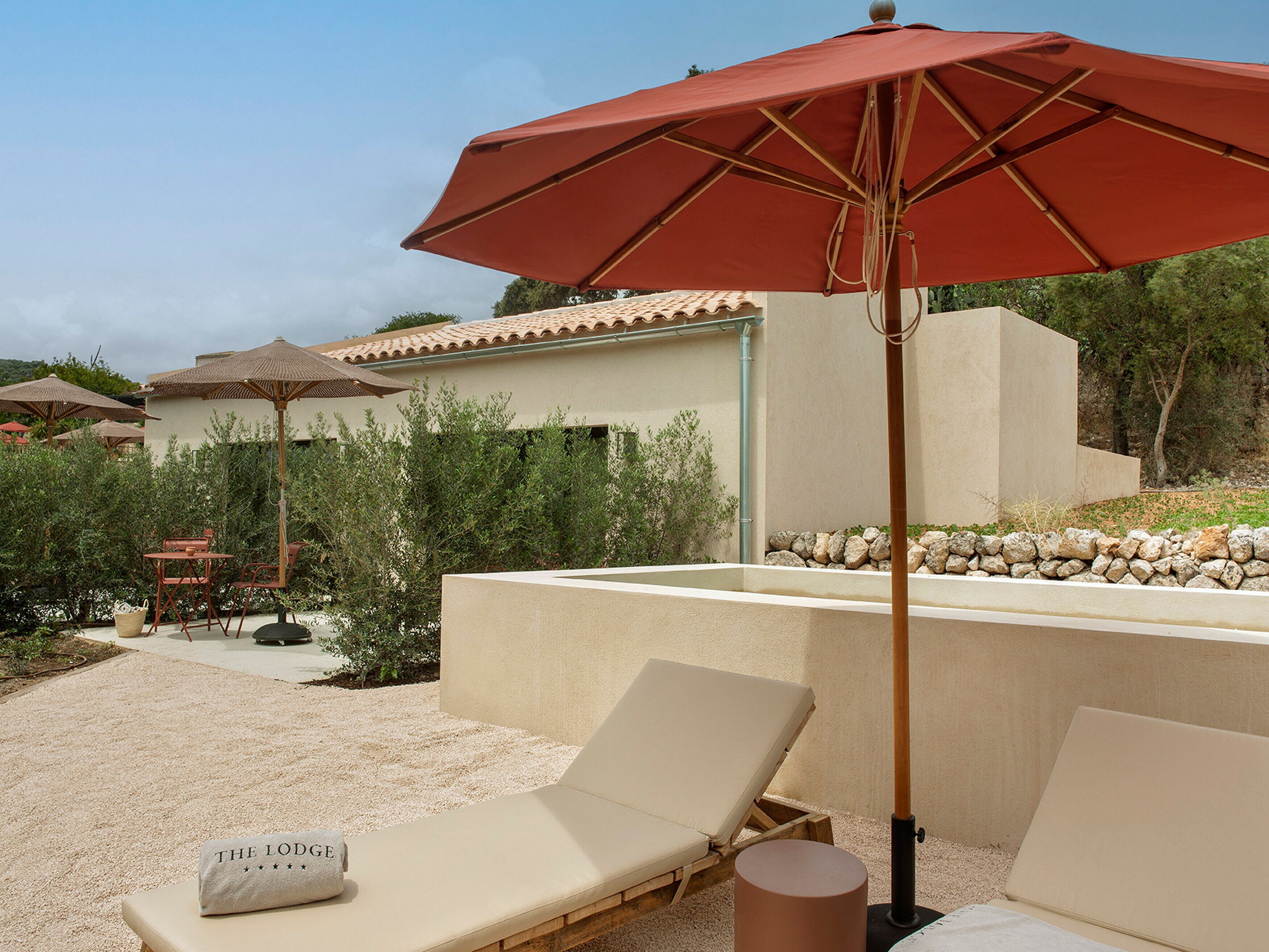 A poolside area with lounge chairs, a red umbrella, and a stone wall.