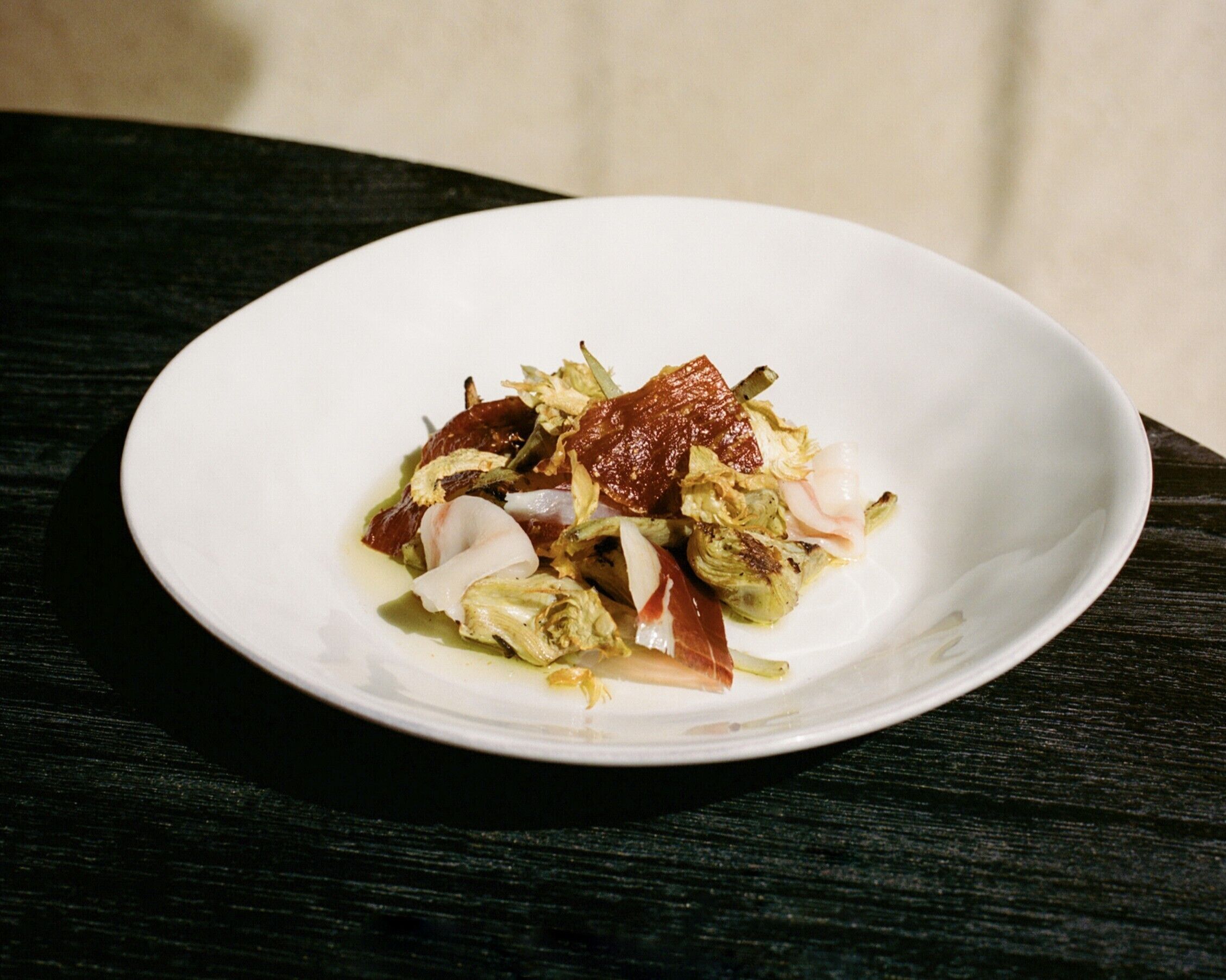 Un plato blanco con ensalada sobre una mesa de madera oscura.