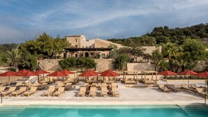 A poolside area with lounge chairs and umbrellas, a pool, and a building with a stone facade in the background. - The Lodge Mallorca - Small Luxury Hotels (Sa Pobla)