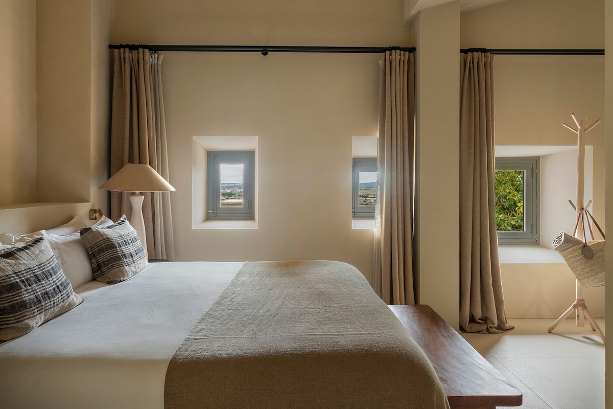 A bedroom with a large bed, two windows, a lamp, and a coat rack.