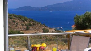 Un balcón con una mesa preparada para el desayuno, con vistas a la costa, montañas y el mar.