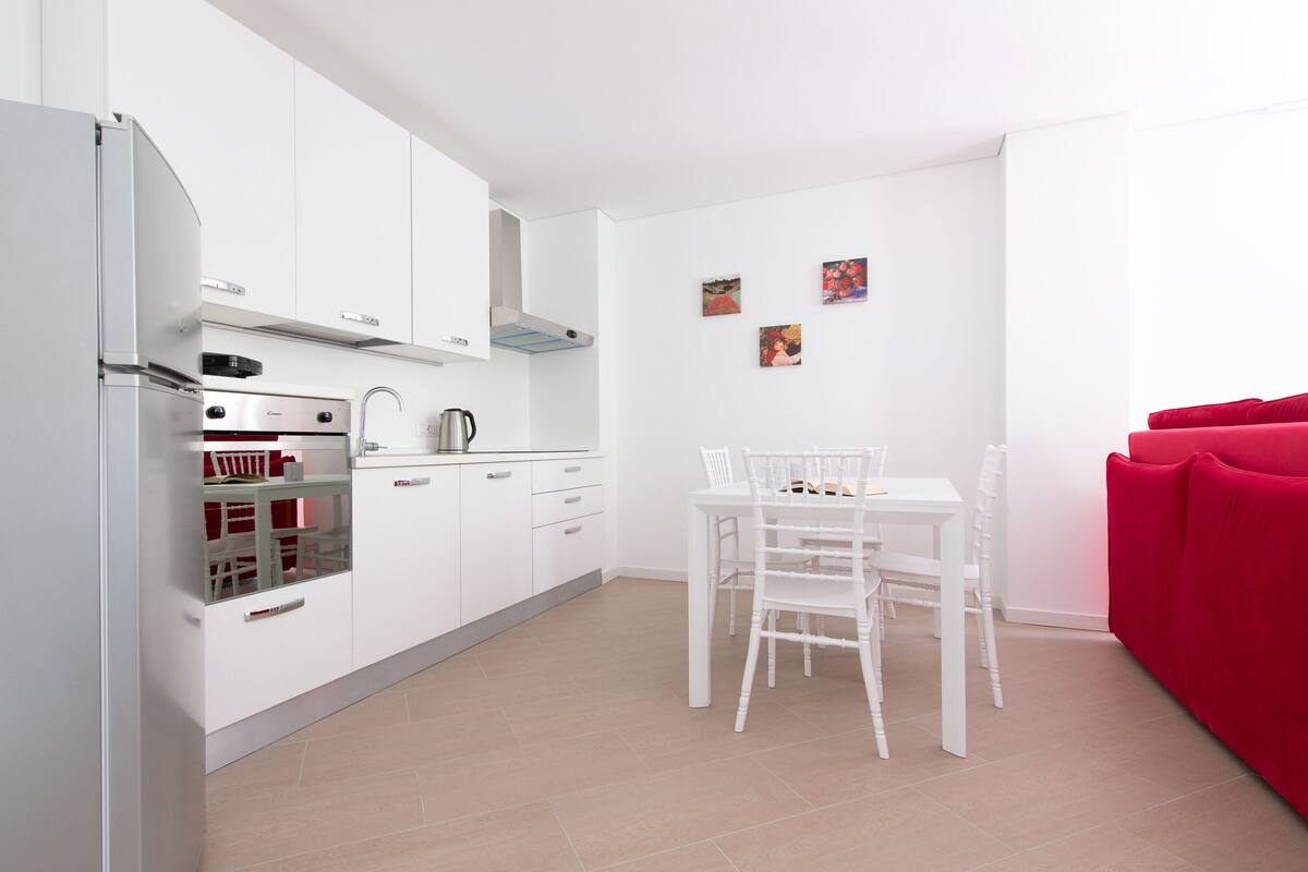 A modern kitchen with white cabinetry, a built-in oven, and a dining area with a white table and chairs.