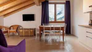 A cozy room with a wooden ceiling, a dining table with chairs, a TV mounted on the wall, and a window with curtains. - Italianway - Villa Tola (Valdisotto)