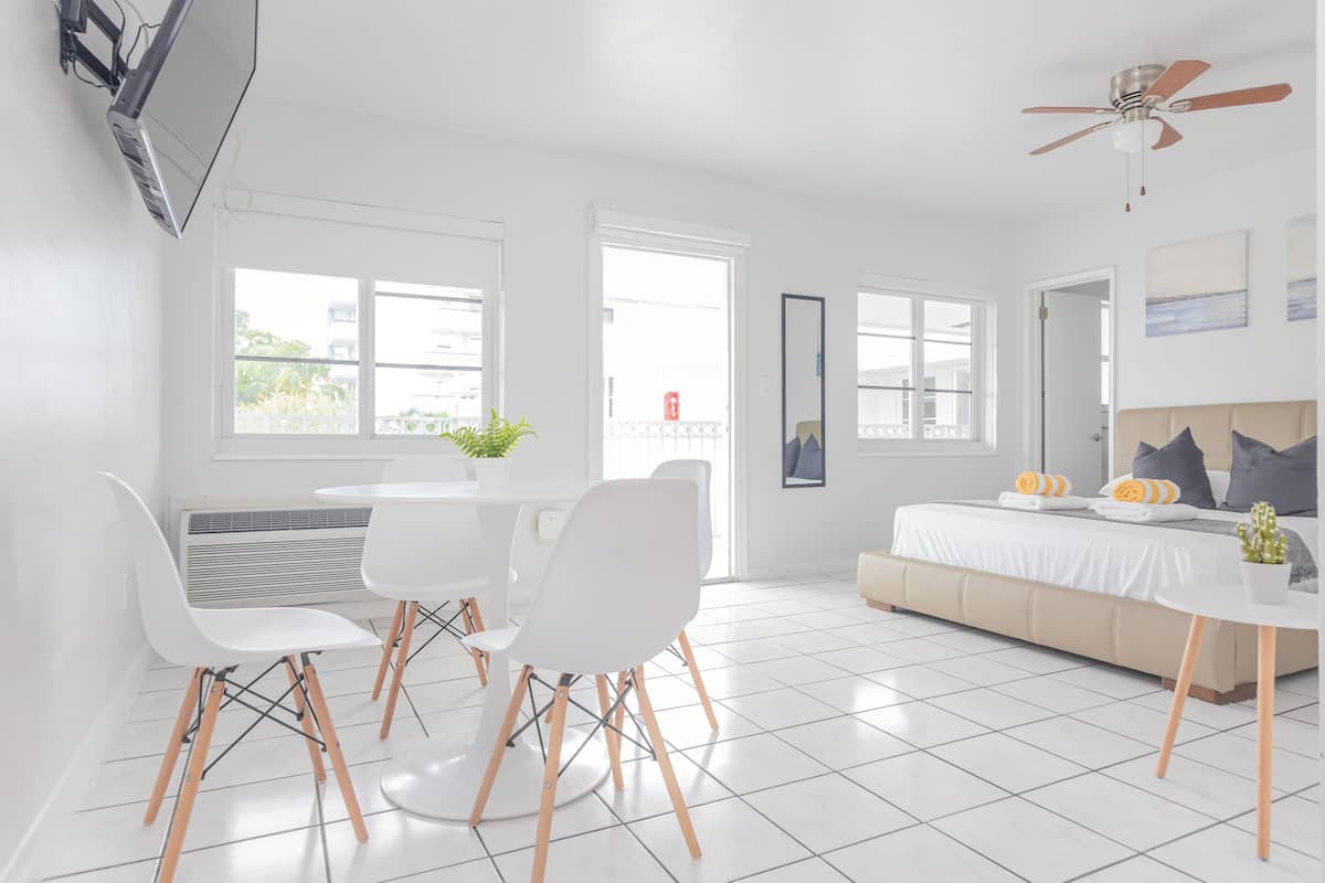 A bright, modern room with a bed, a dining table with chairs, and a ceiling fan.