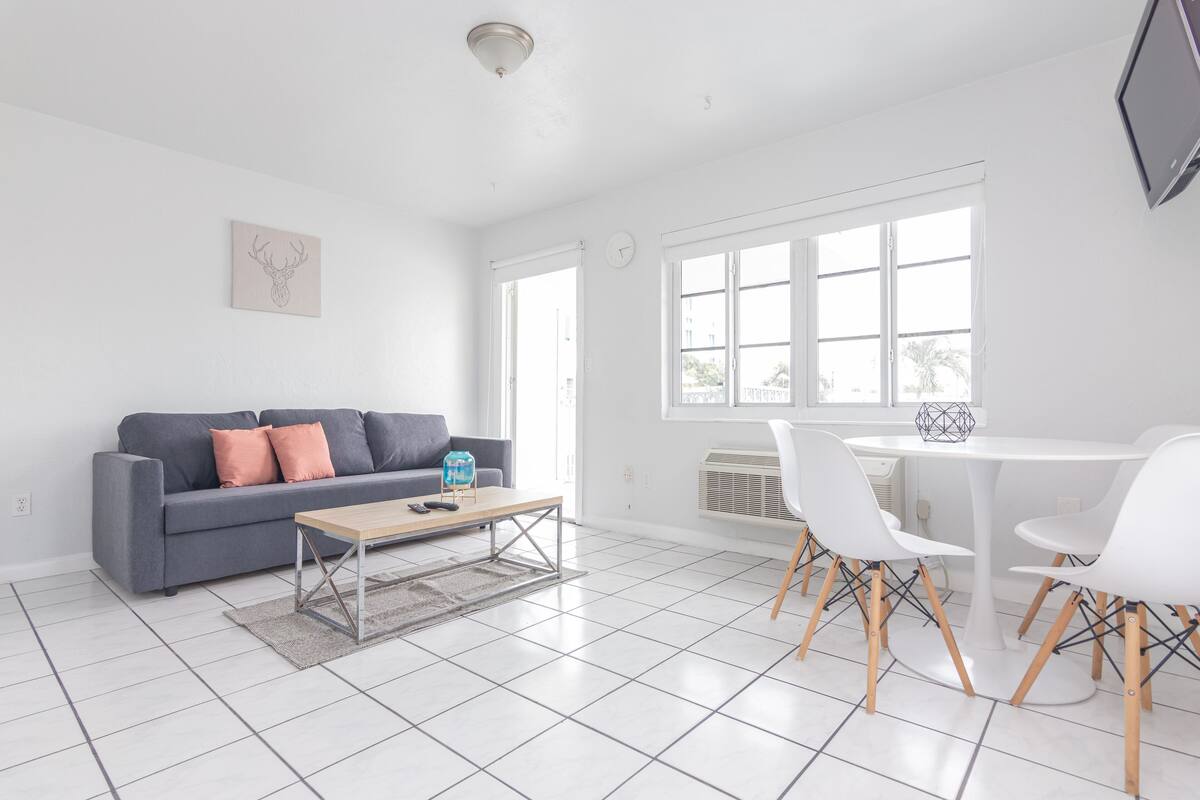 A spacious living area with a grey sofa, a coffee table, and a dining table with chairs.