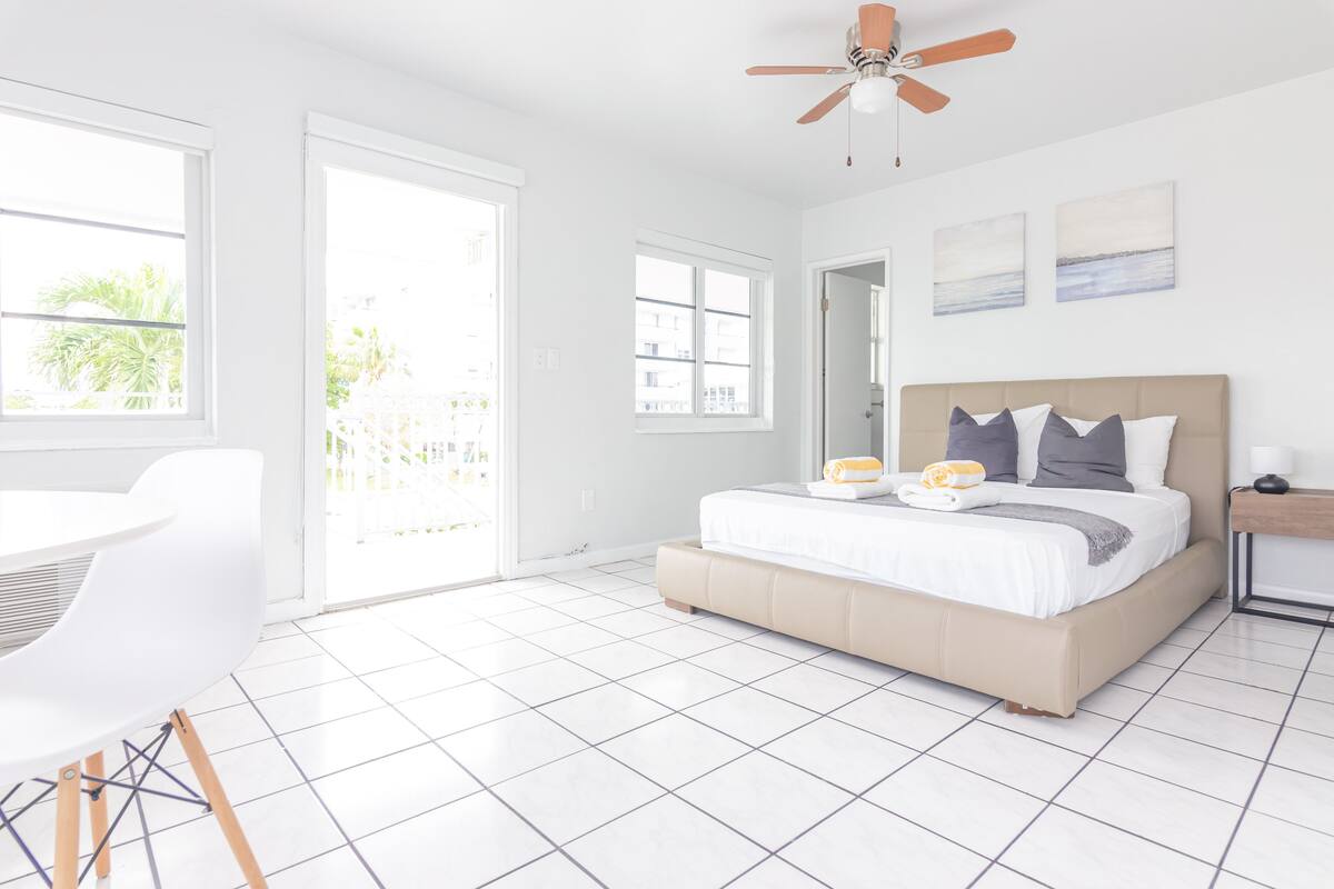 A bright bedroom with a bed, a ceiling fan, and a view through the door.