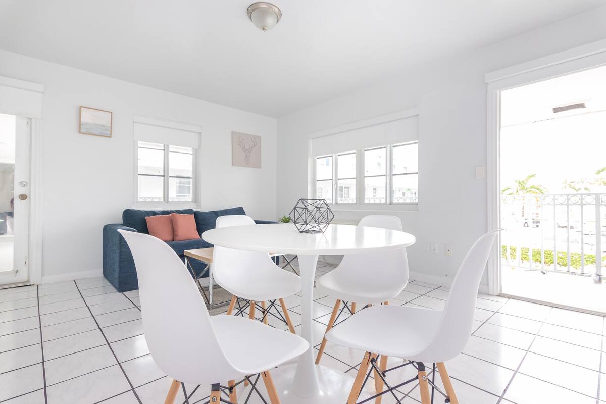 A modern living room with a white round table, white chairs, a blue sofa, and a large window.