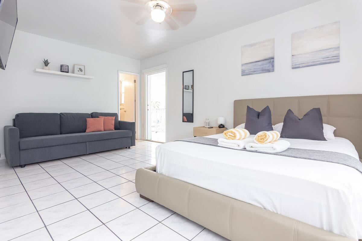 A modern bedroom with a large bed, a grey sofa, and a small table with a lamp.