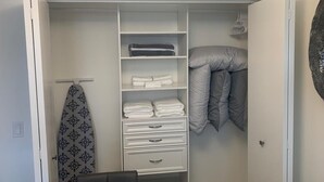 Un vestidor con repisas para ropa doblada, un perchero para una tabla de surf y una cama con ropa de cama gris.