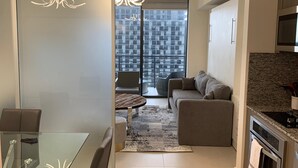 Un apartamento moderno con una mesa de comedor de vidrio, un sofá, una alfombra pequeña y una cocina con encimeras de granito.