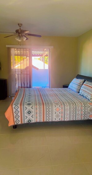 A bedroom with a bed, a ceiling fan, and a view of the outside through a door.