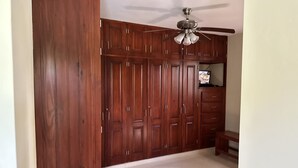 Une pièce avec des armoires en bois, un ventilateur de plafond et un téléviseur posé sur un meuble.