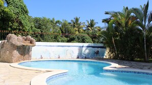 Une piscine ornée d’une fresque murale, entourée de palmiers et d’un mur de pierre.