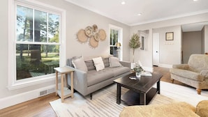 A spacious living room with a grey sofa, a coffee table, and a patterned armchair. - Charm of SouthPark - 5 Bedrooms - 1 of a Kind Lot! (Charlotte)