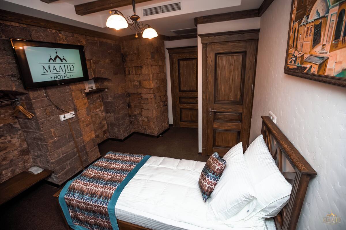 Una habitación de hotel con una cama, un televisor montado en la pared y una puerta de madera.