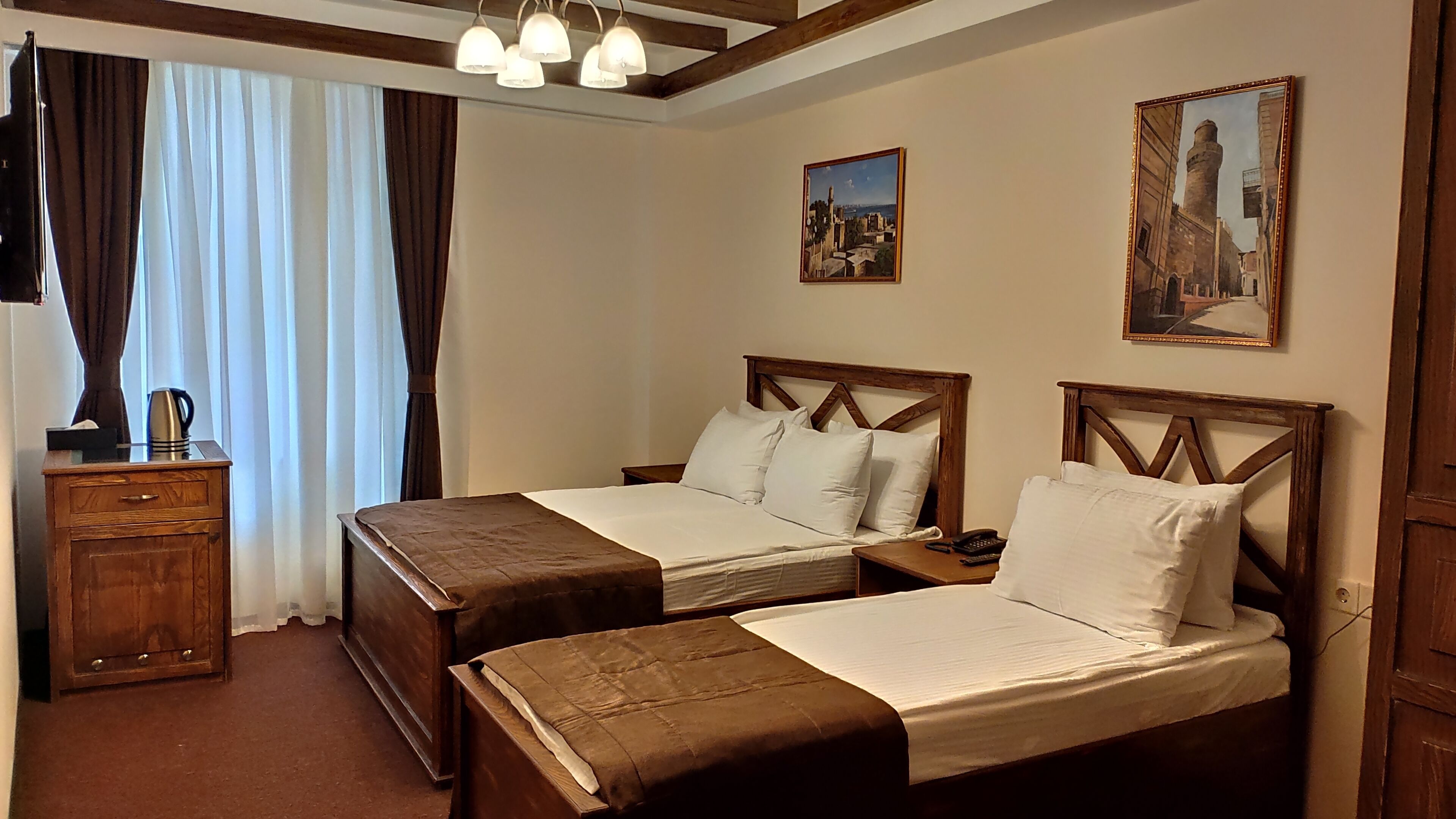 A hotel room with two beds, a wooden nightstand, a coffee maker, and two paintings on the wall.