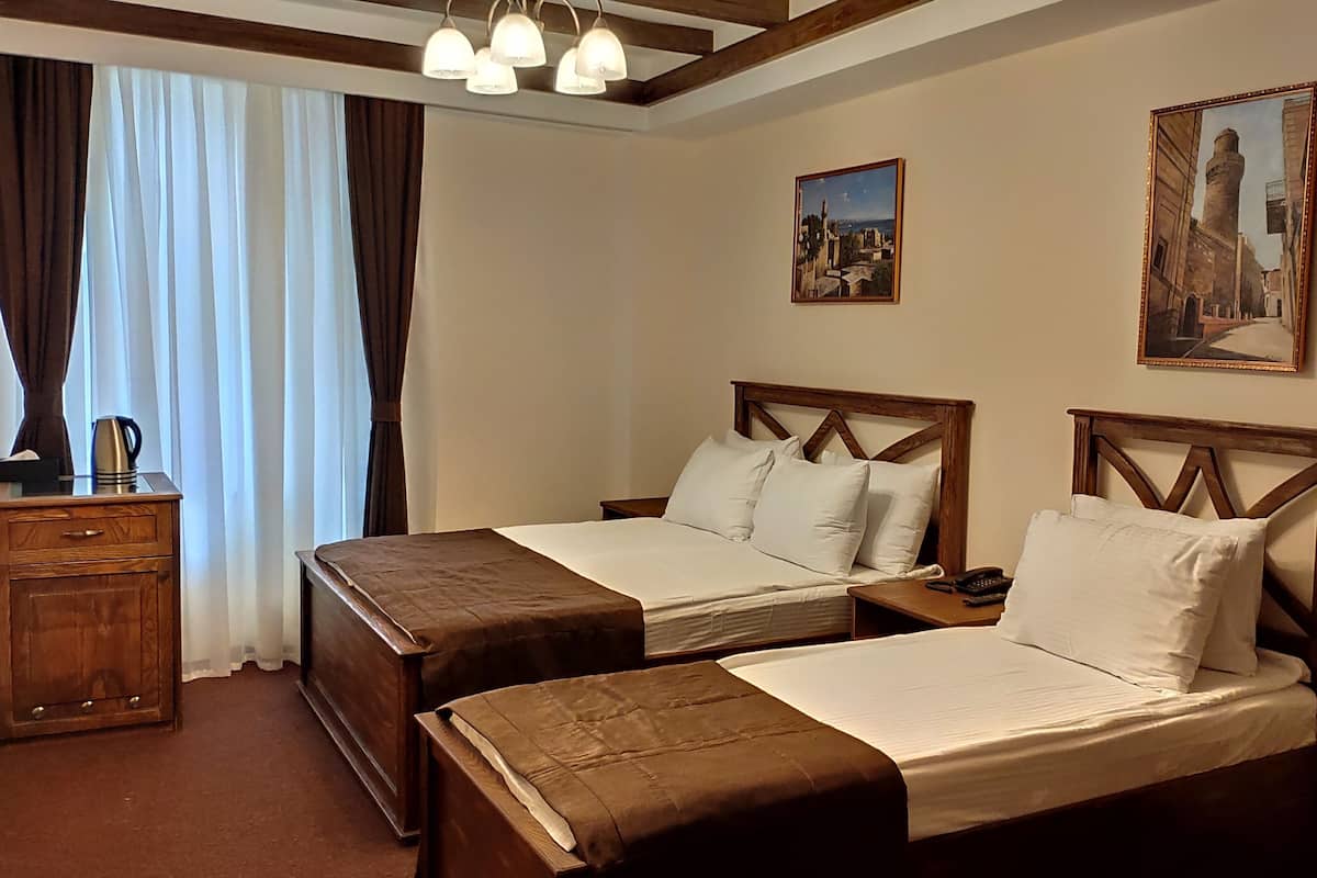 Habitación de hotel con dos camas, una mesita de noche de madera, una cafetera y dos cuadros en la pared.