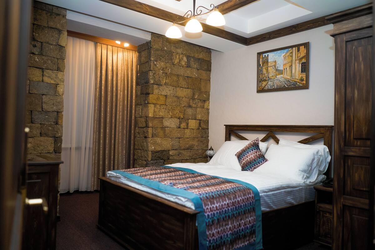 Un dormitorio con pared de piedra, una cama con colcha estampada, un cuadro en la pared y cabecera de madera.