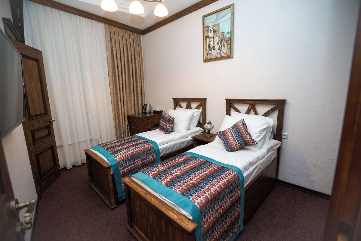 Una habitación de hotel con dos camas de madera, un armario de madera, un cuadro en la pared y una ventana con cortinas.