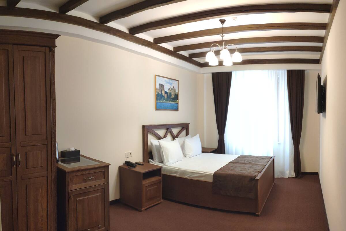 Habitación de hotel con una cama grande, armario de madera, mesita de noche y un cuadro en la pared.