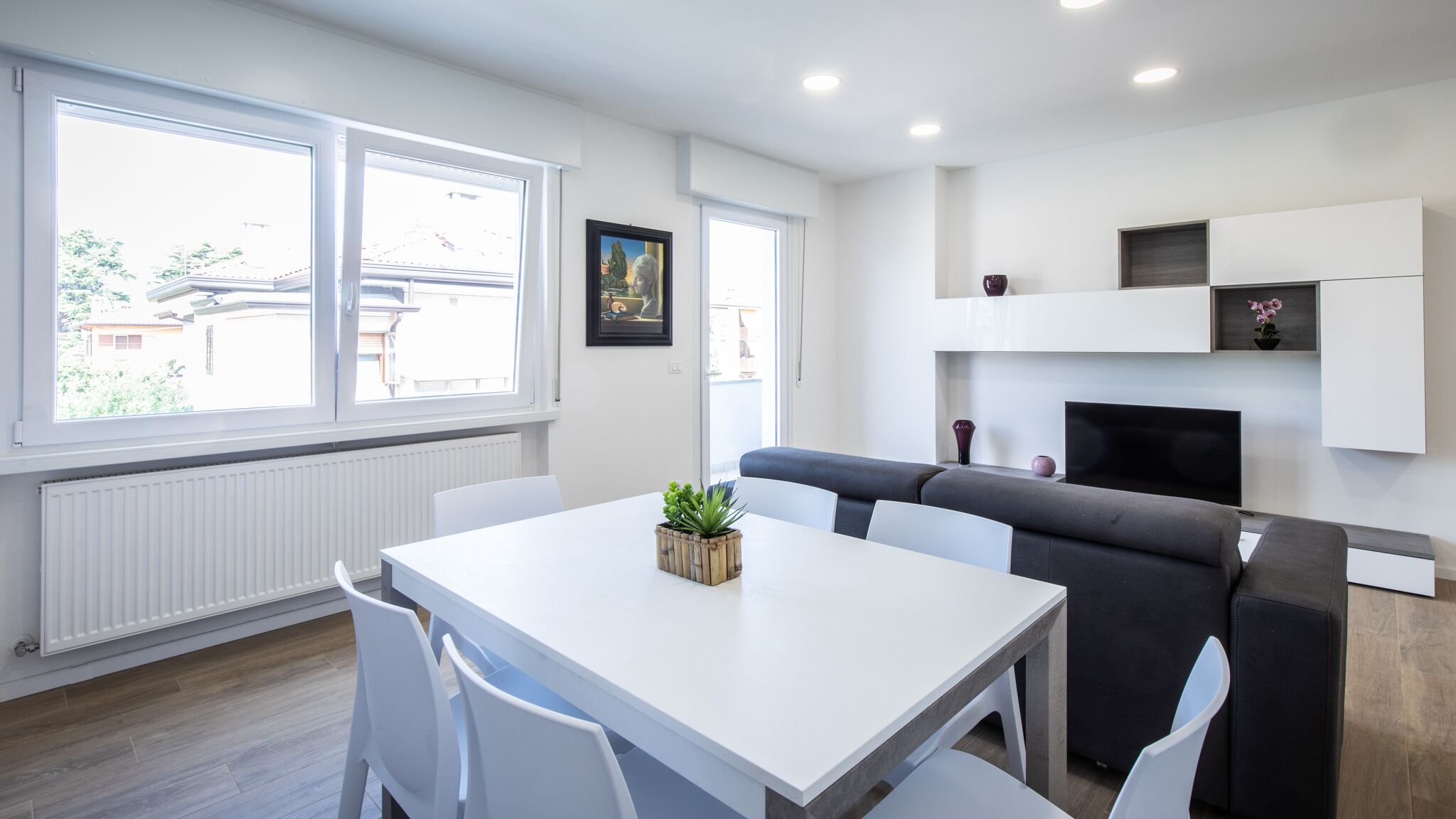A modern, well-lit living room with a white table, grey sofa, and a TV.