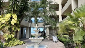 Un patio con una fuente en el centro, rodeado de palmeras y un edificio con varios balcones.