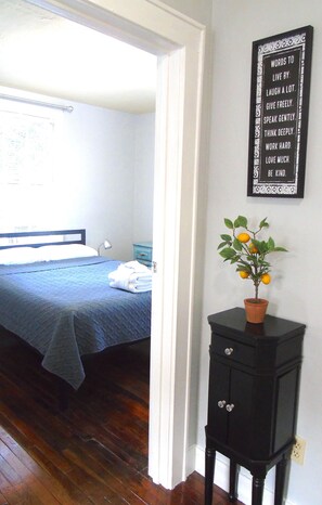 A bedroom with a bed, a nightstand, a potted plant, and a wall with inspirational words. - Lovely Gem! 10 mins to Downtown Charleston & Very Affordable! (North Charleston)