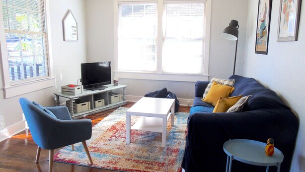 Un salon avec un canapé bleu, une table basse blanche, un fauteuil bleu, une petite table d’appoint et un téléviseur posé sur un meuble.