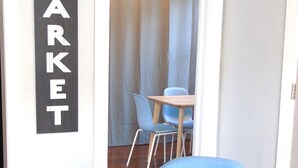 Une pièce avec un fauteuil bleu, un plancher en bois, un panneau indiquant « MARCHÉ » sur le mur, et un coin repas à l’arrière-plan.