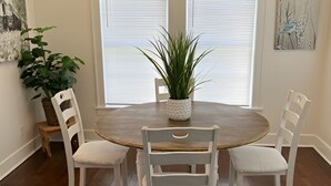 Un comedor con una mesa redonda de madera, cuatro sillas blancas tapizadas y una planta en maceta.