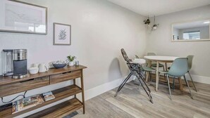 A modern dining area with a wooden table and chairs, a coffee machine, and framed artwork on the wall. - Institute Charm! King Studio w/ Kitchen & Smart TV (Colorado Springs)