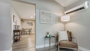 A modern living room with a brown leather sofa, a small round table with a lamp, and a large air conditioning unit on the wall. - Institute Charm! King Studio w/ Kitchen & Smart TV (Colorado Springs)